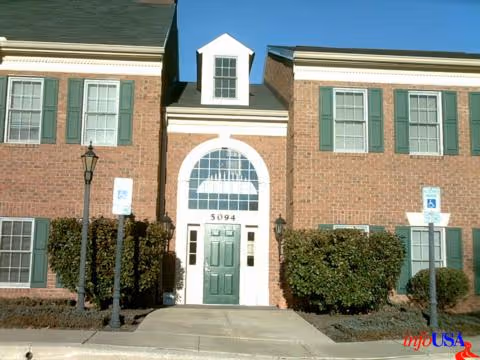 Exterior brick senior living facility with green doors, arched window, hedges, and handicap signs.