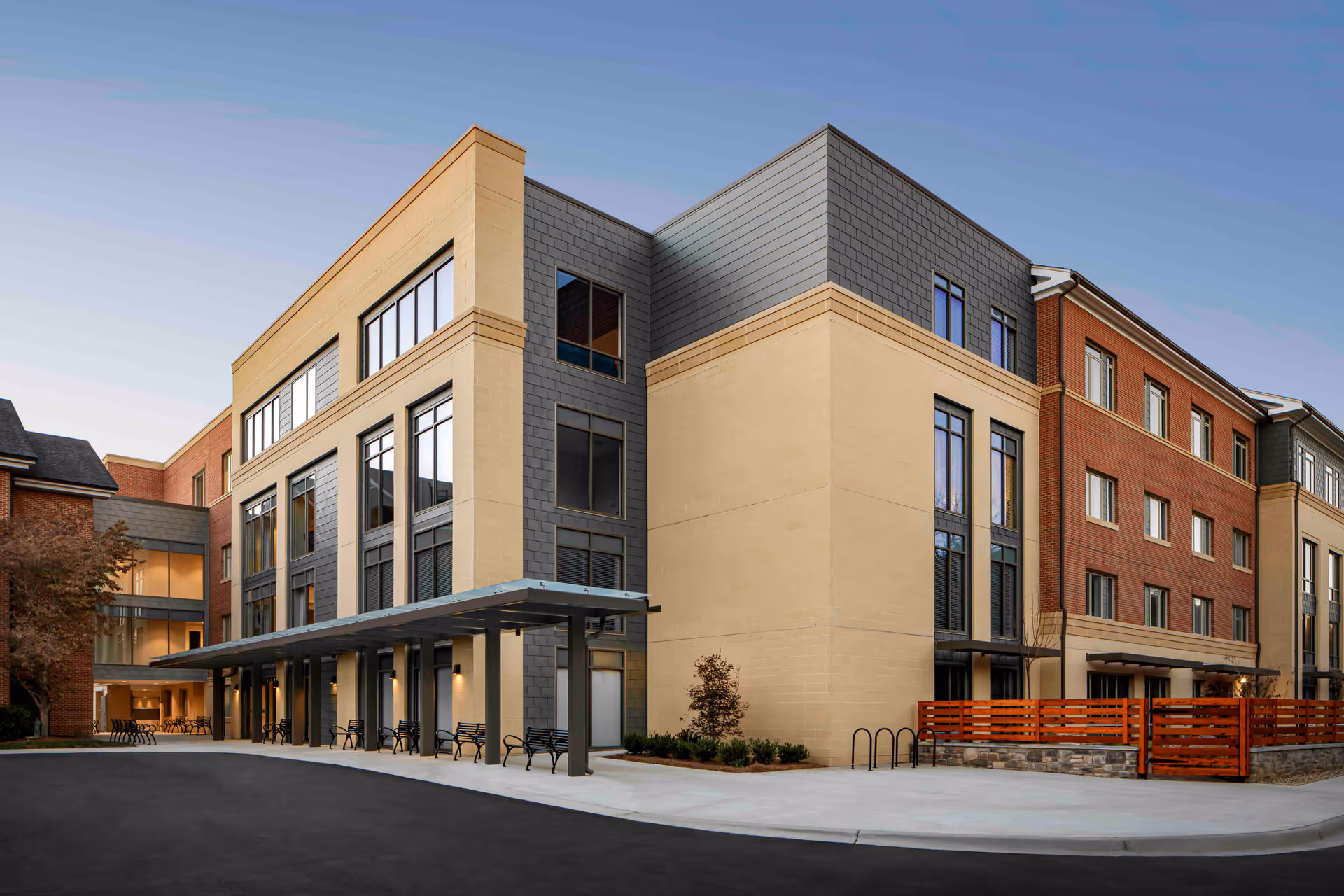 Modern multi-story senior living building exterior with a covered entrance, benches, and large windows.