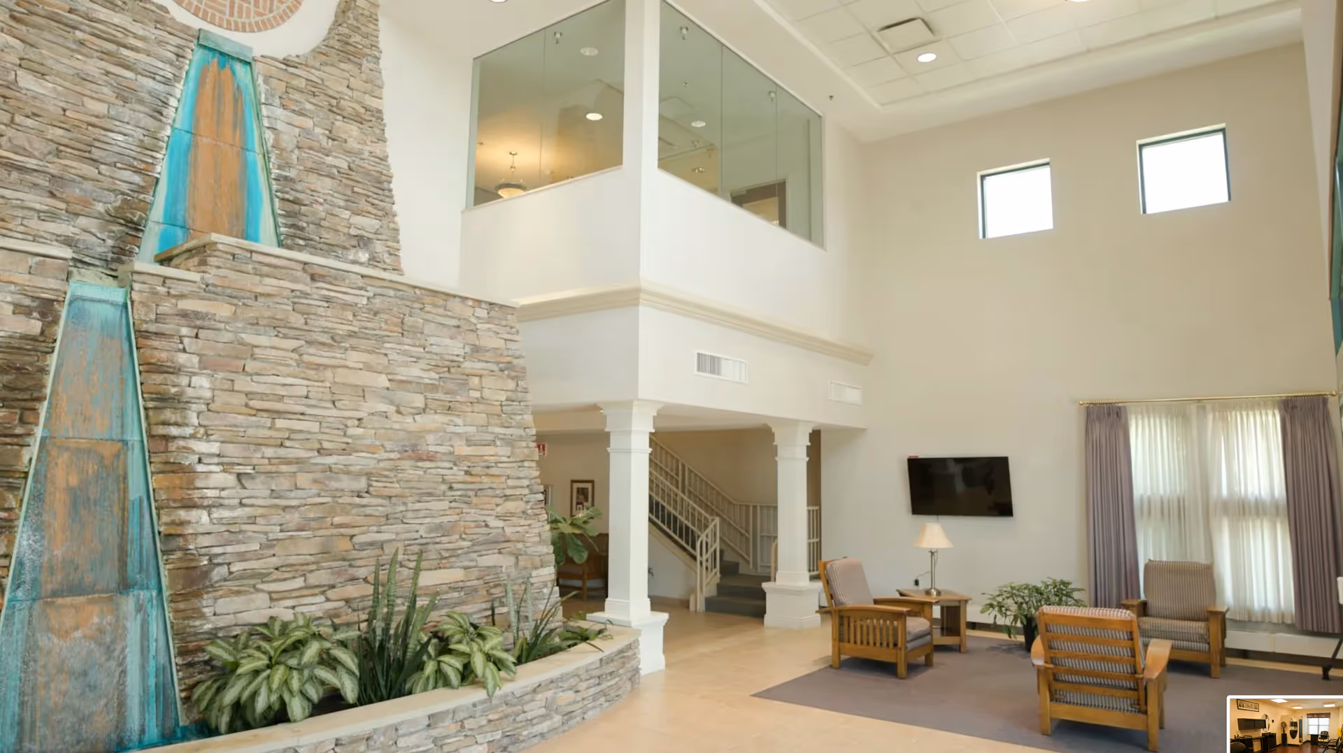 Spacious interior lobby with a stone waterfall feature, glass-railed mezzanine, and comfortable seating.