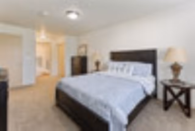 Bedroom with a large bed, nightstands, lamps, and a doorway to a hallway.