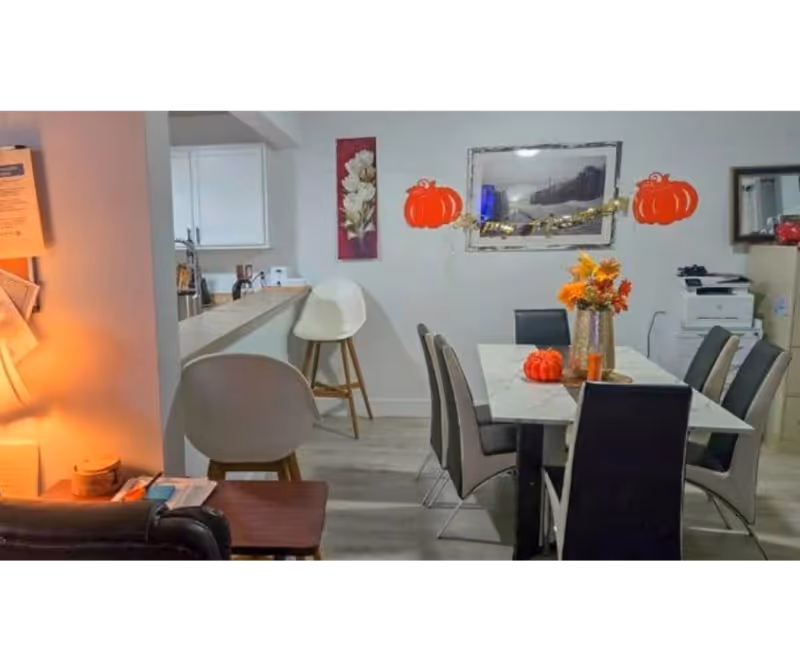Interior dining room with a white table, gray chairs, pumpkins, and a kitchenette bar.