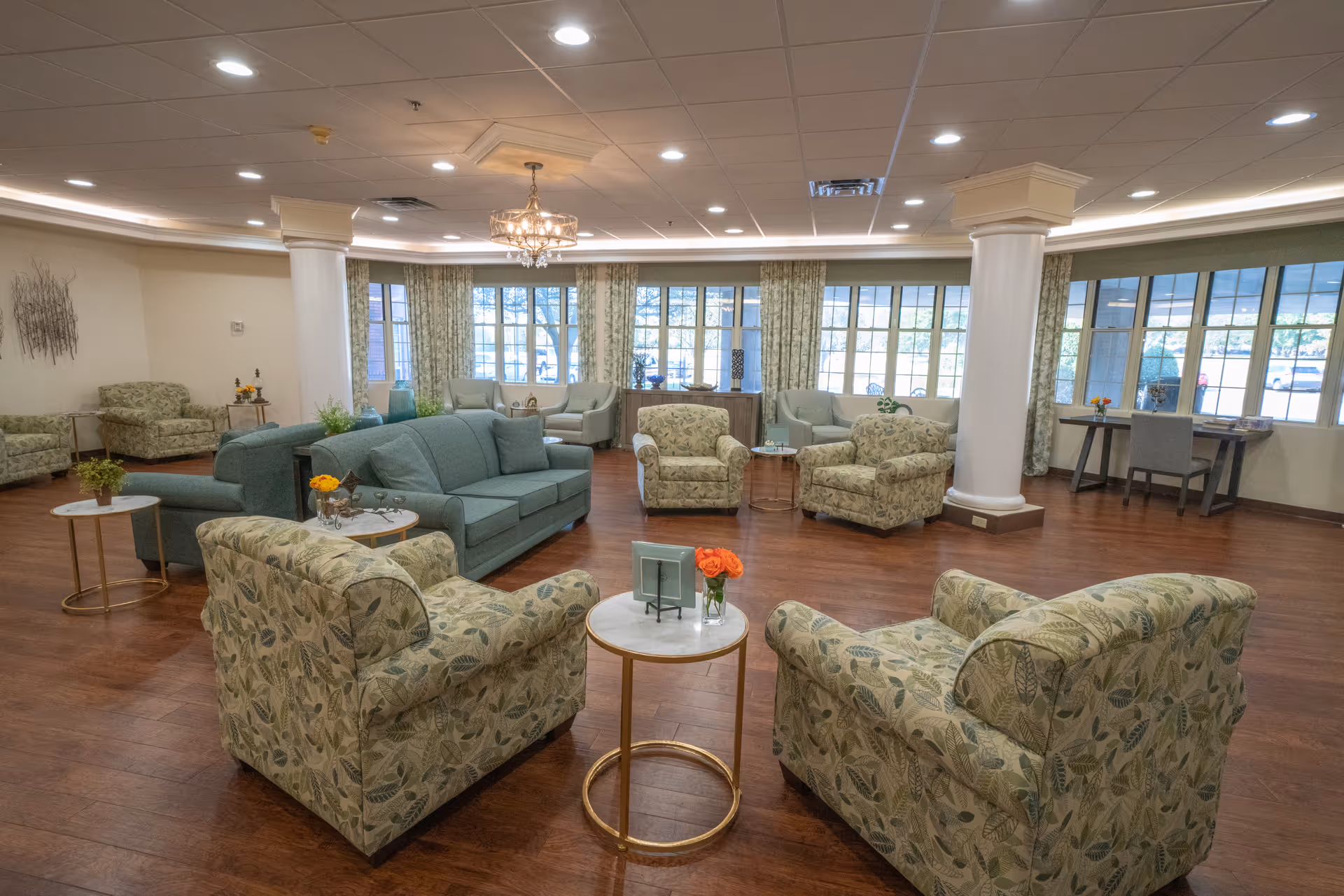 Spacious senior living lounge with patterned armchairs, couches, and large windows.