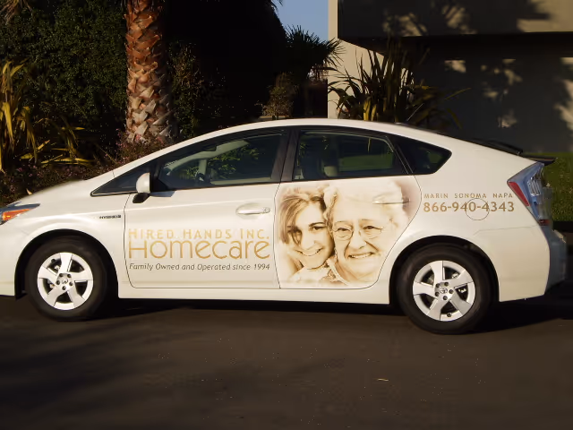 A white branded Hired Hands Homecare van parked outside a building with palm trees.