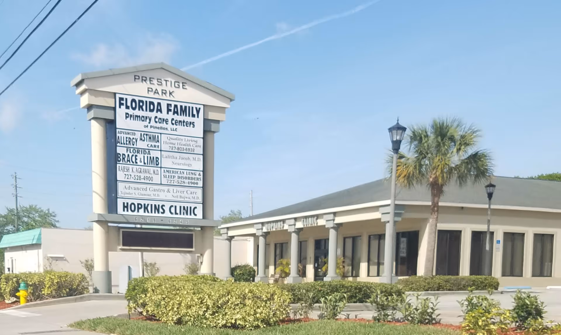 Exterior view of a single-story clinic with a tall signboard and palm trees.