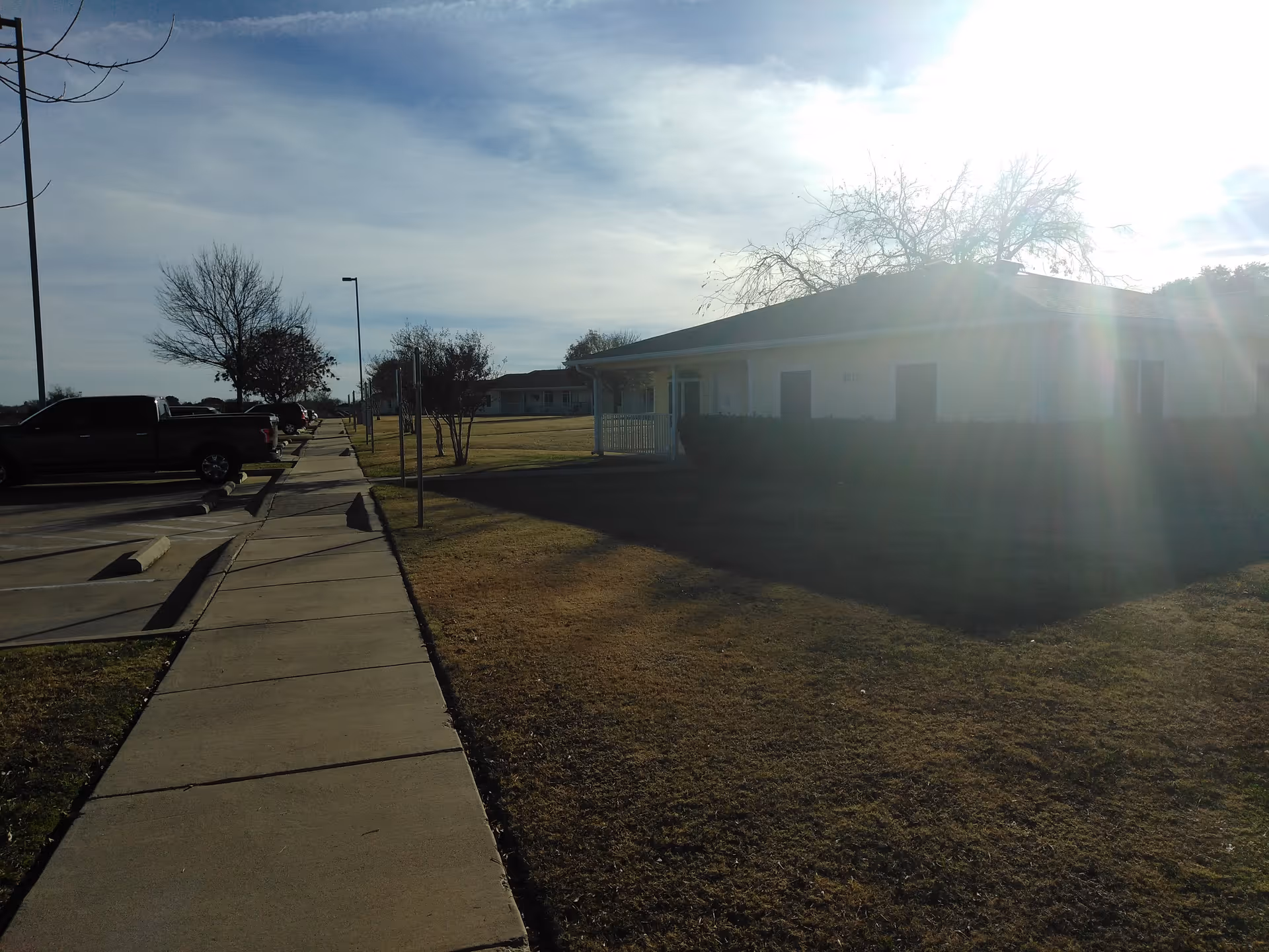 Exterior of Tremont Terrace senior living facility, featuring a sidewalk, parked cars, and sunny lawn.