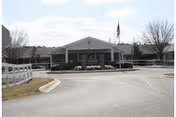 Front view of Lake Park of Madison Nursing and Rehabilitation entrance with flag and driveway.