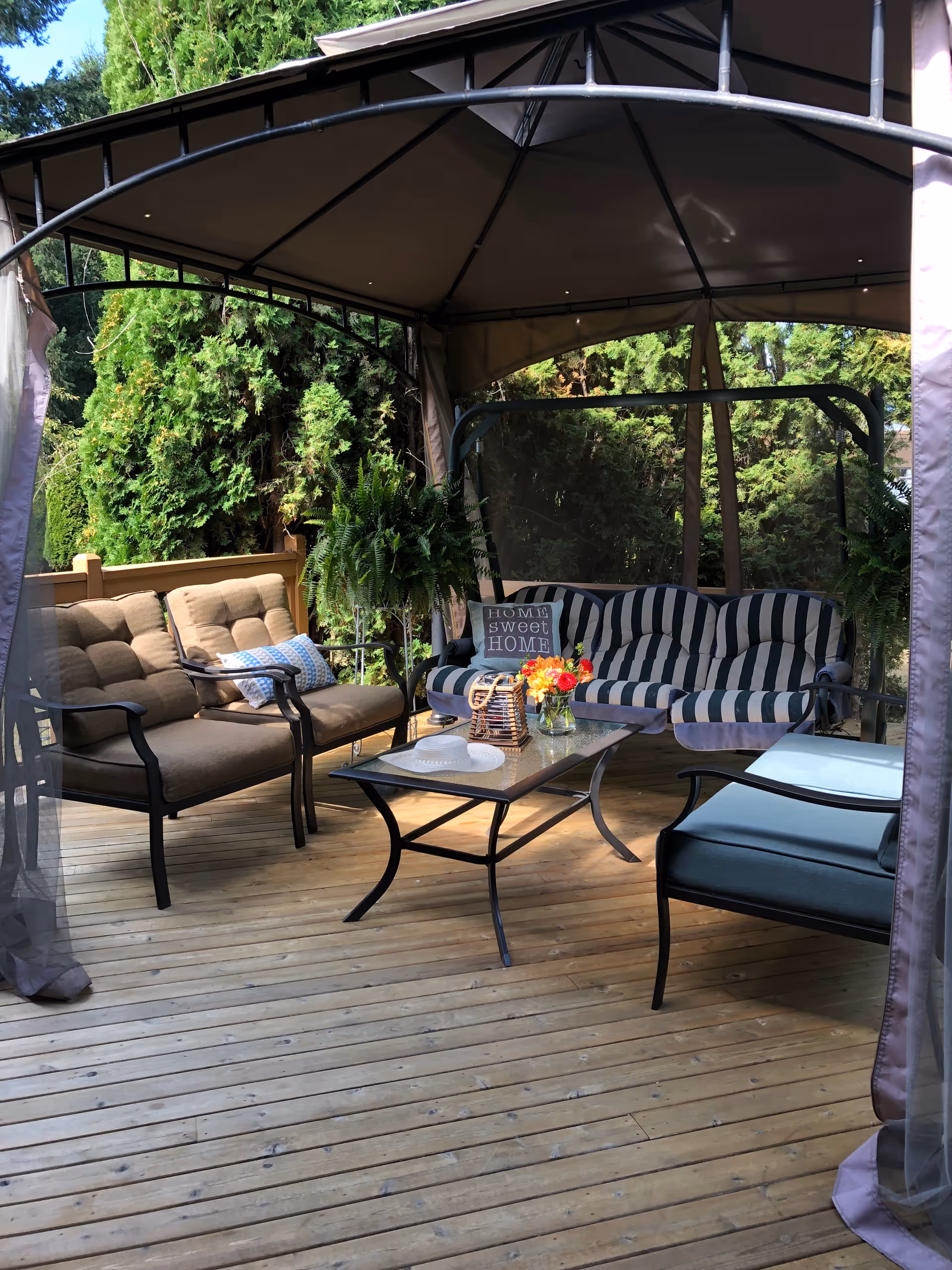 Covered outdoor deck with cushioned seating, a glass table, and potted plants.