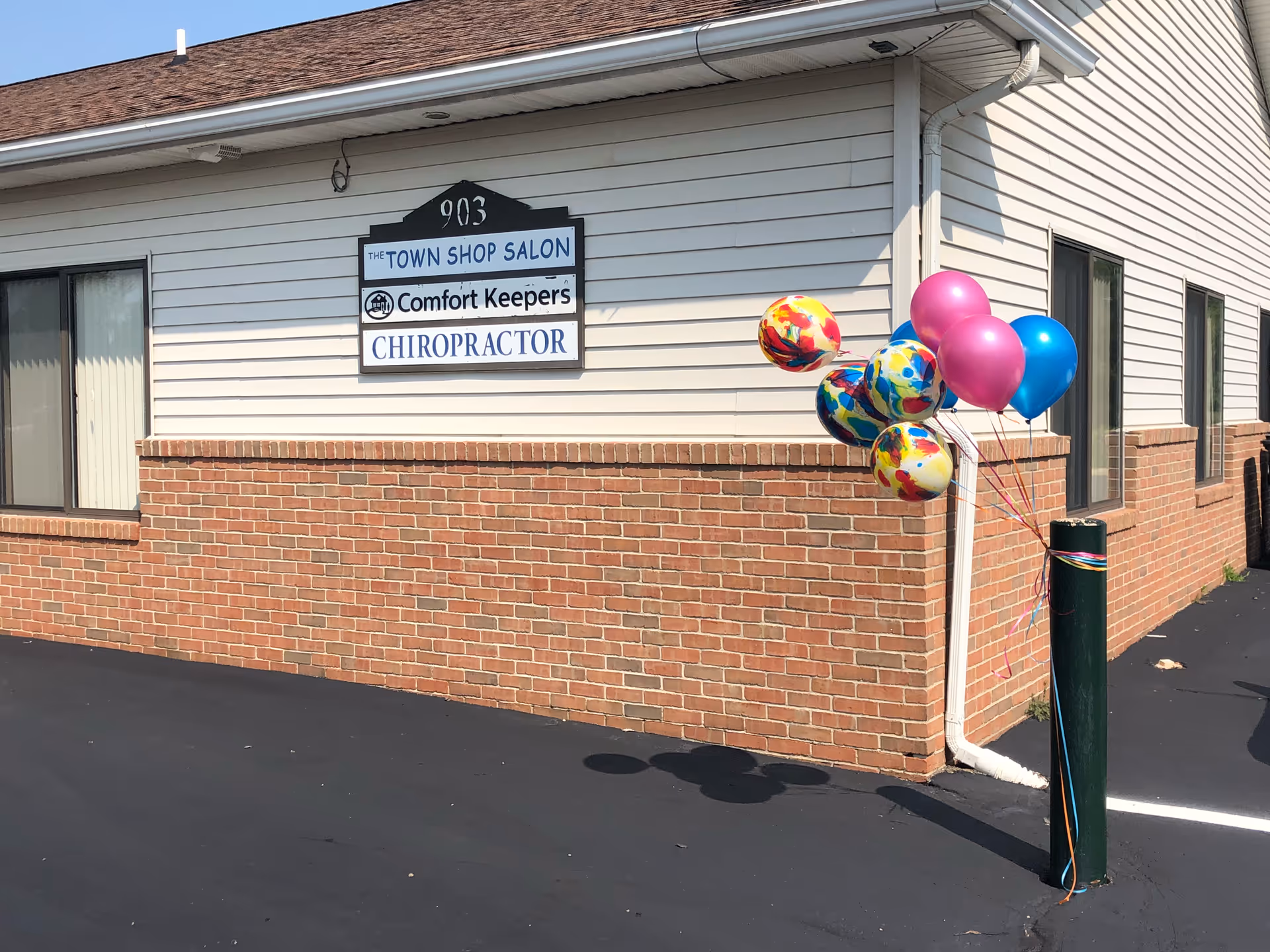 Exterior view of Comfort Keepers building with sign, balloons, and brick lower wall.
