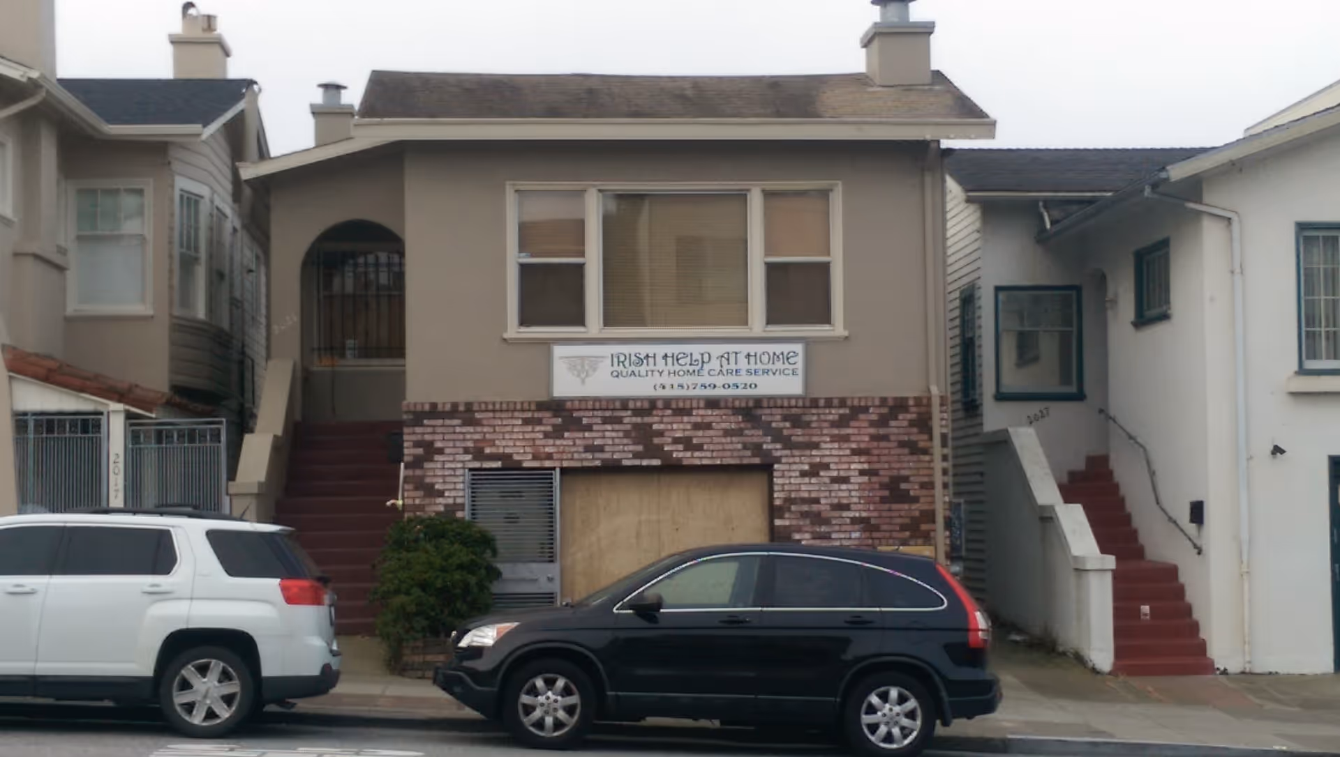 Two-story beige building with 'Irish Help At Home' sign and parked cars in front.
