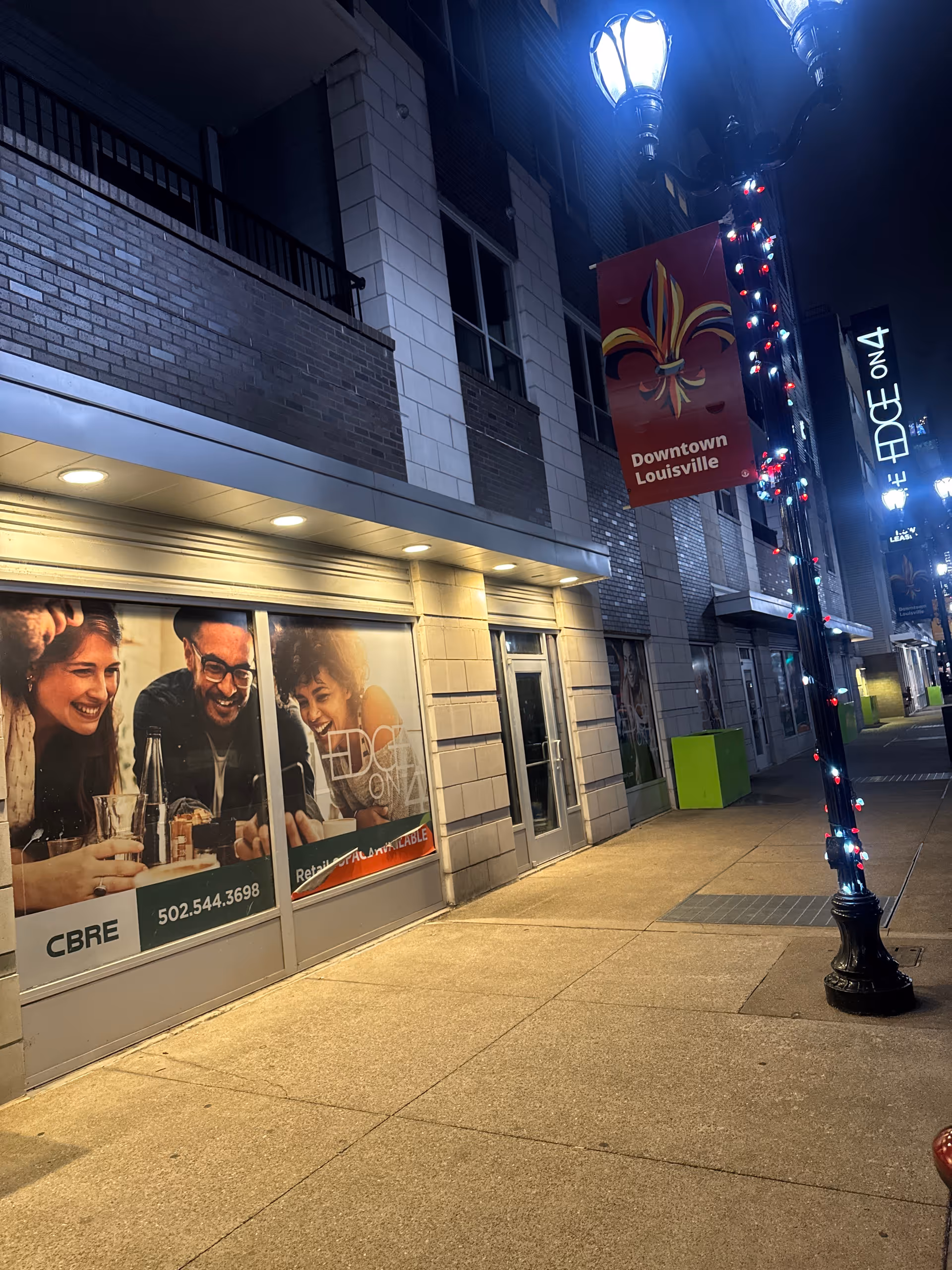 Nighttime street exterior with storefront windows and a Downtown Louisville banner