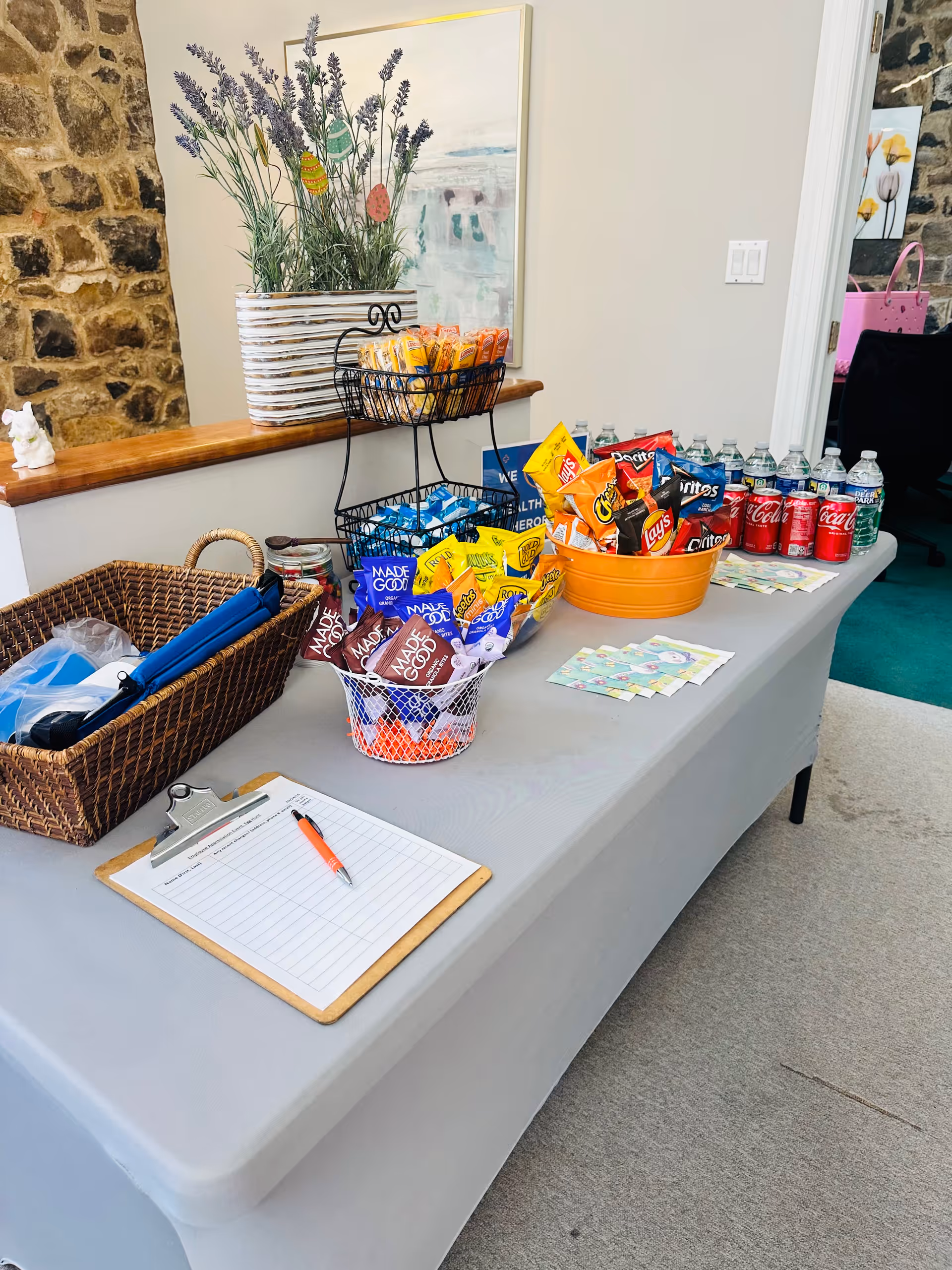 Indoor snack station on a gray table with chips, drinks, and a clipboard.