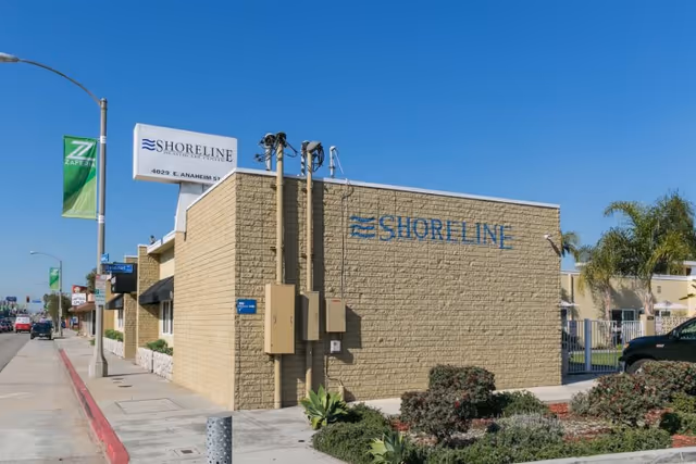 Exterior view of the Shoreline Healthcare Center building with signage on a beige brick wall along a city sidewalk.