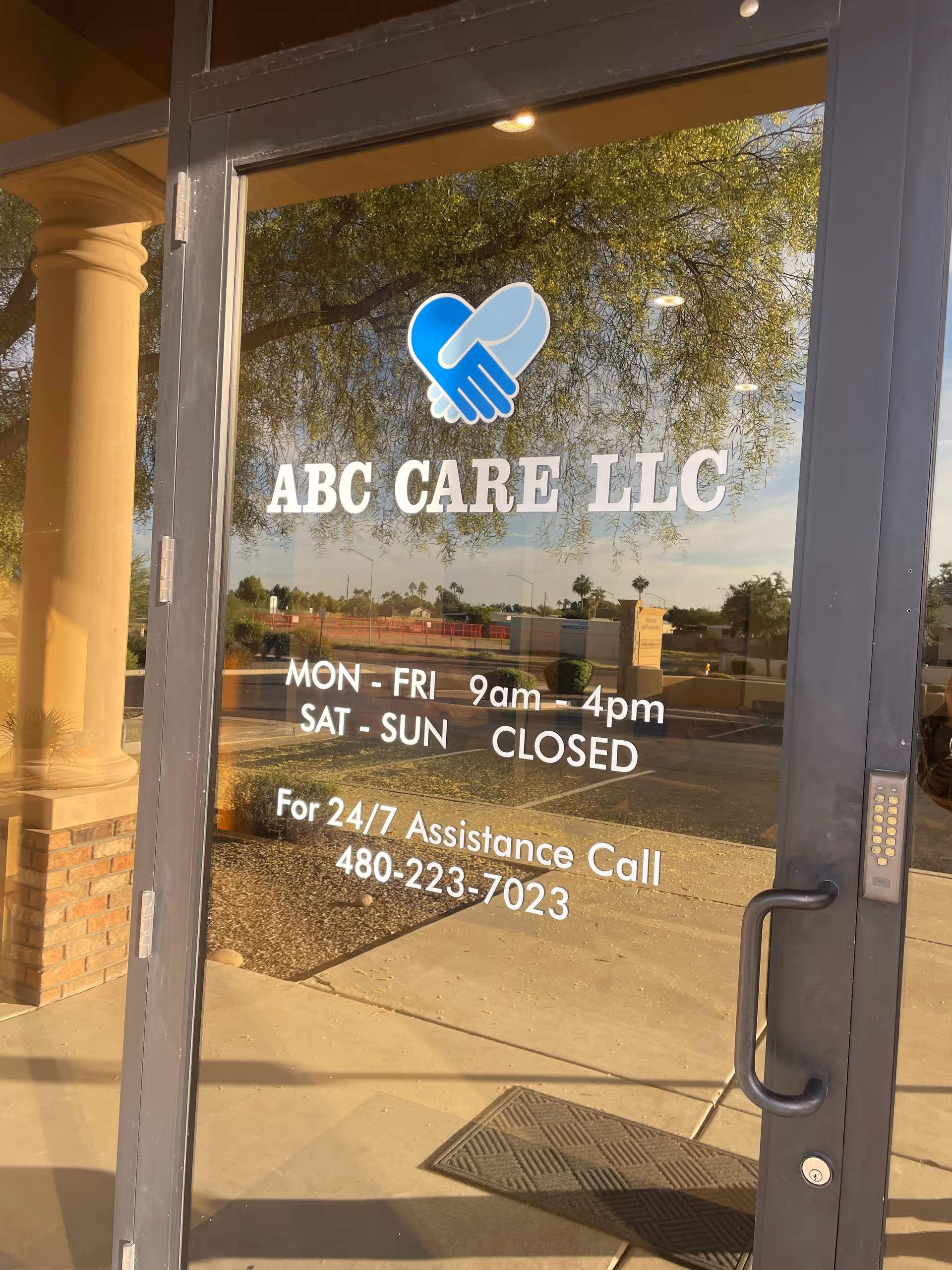 Glass door shows ABC CARE LLC logo, hours, and 24/7 assistance phone number.