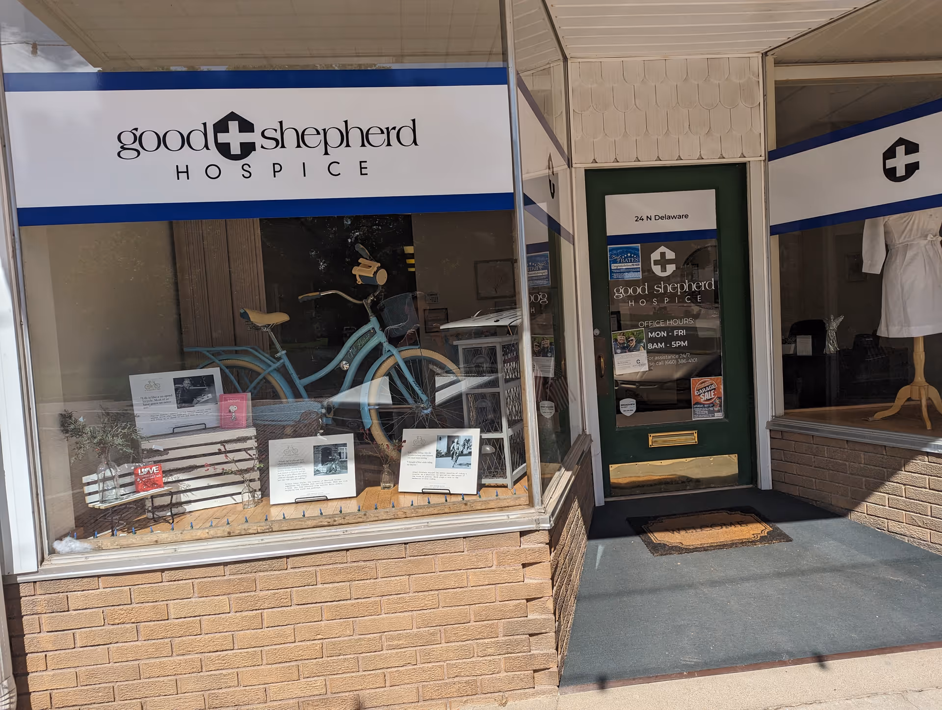Storefront for Good Shepherd Hospice with window display, bicycles, and a green door.
