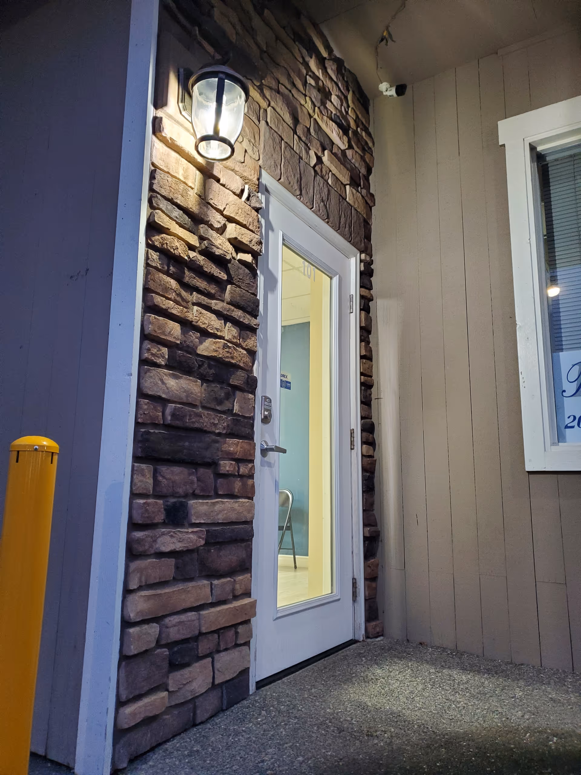Exterior entrance with stone wall, glass door, and mounted porch light