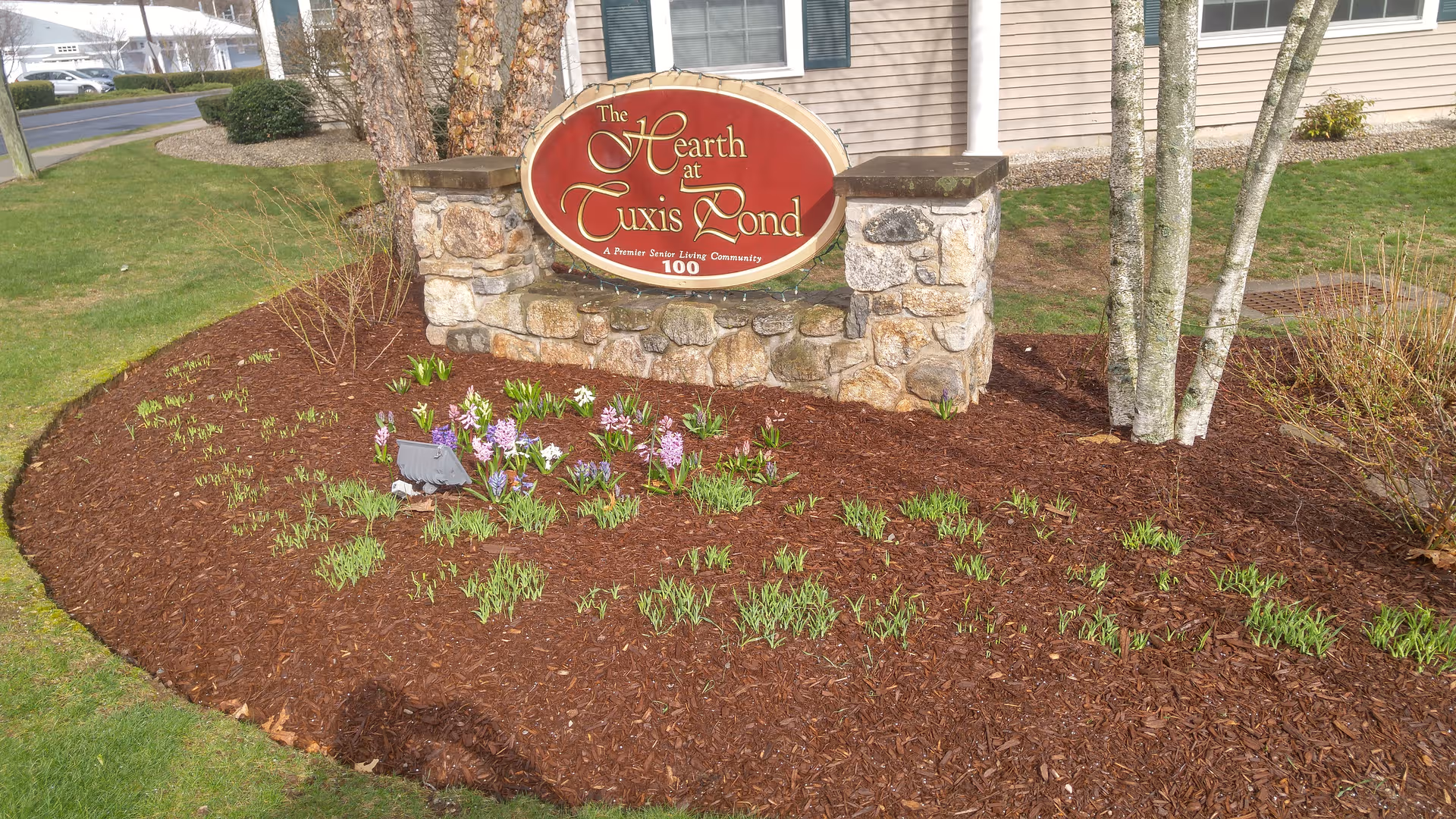 A landscaped entrance with a stone sign and mulch bed in front of a beige building.