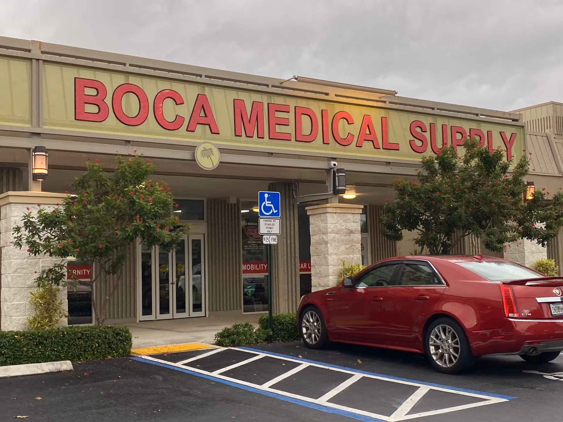 Front of Boca Medical Supply storefront with large red sign and a parked red car.