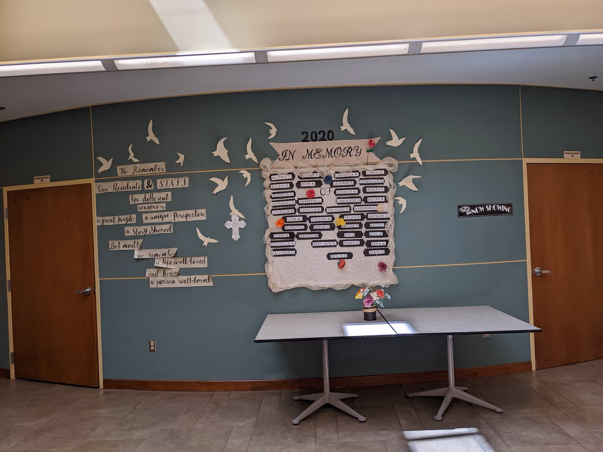 Memorial display on a blue wall with dove shapes and a table.