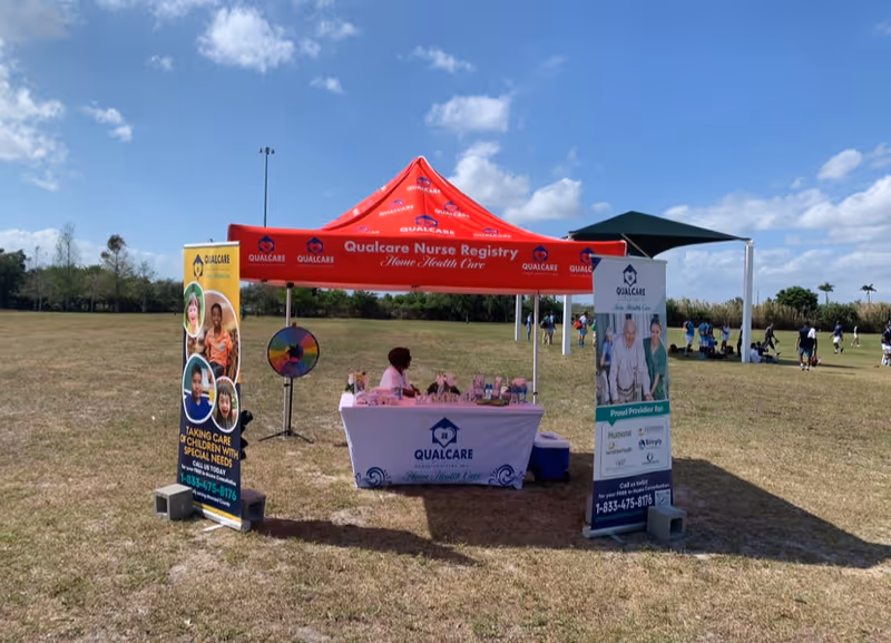 Outdoor health fair booth for Qualcare Nurse Registry with banners and a spinning wheel.