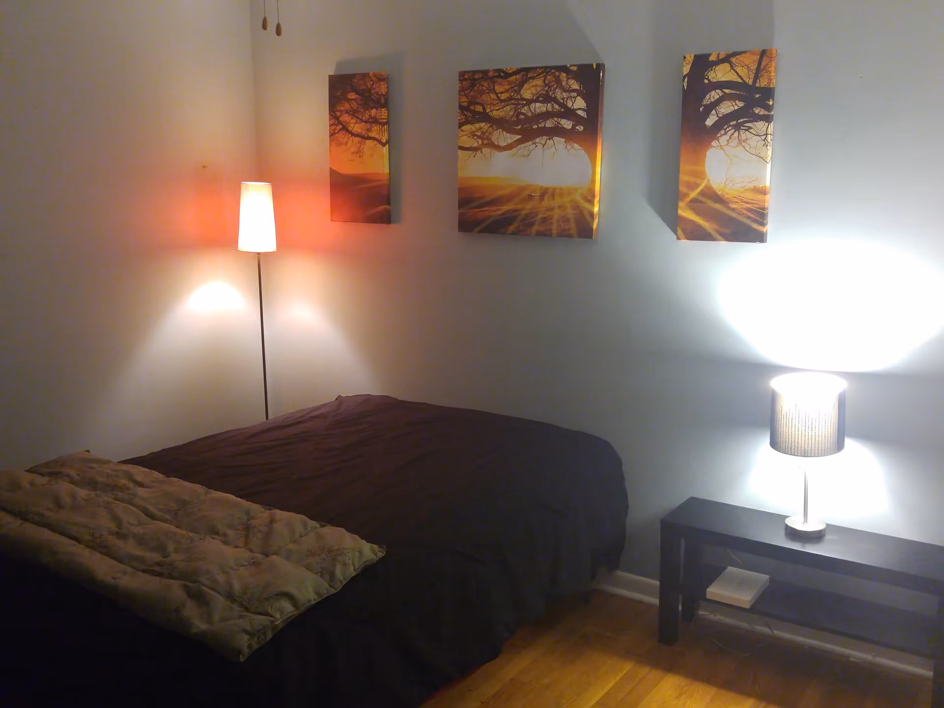 Bedroom in Wind Gap Manor with a bed, two lamps, and three-panel tree-sunset wall art.