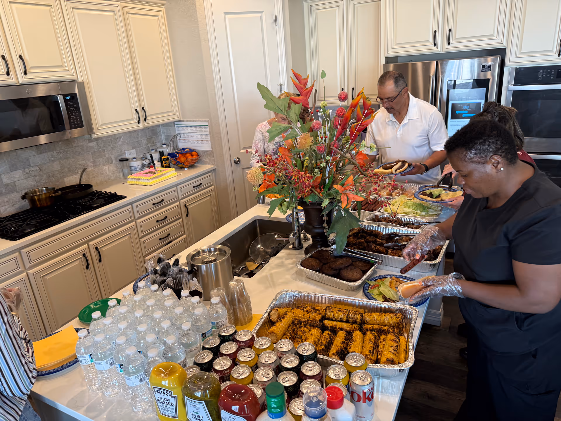 Two staffers set up a buffet in a bright kitchen.