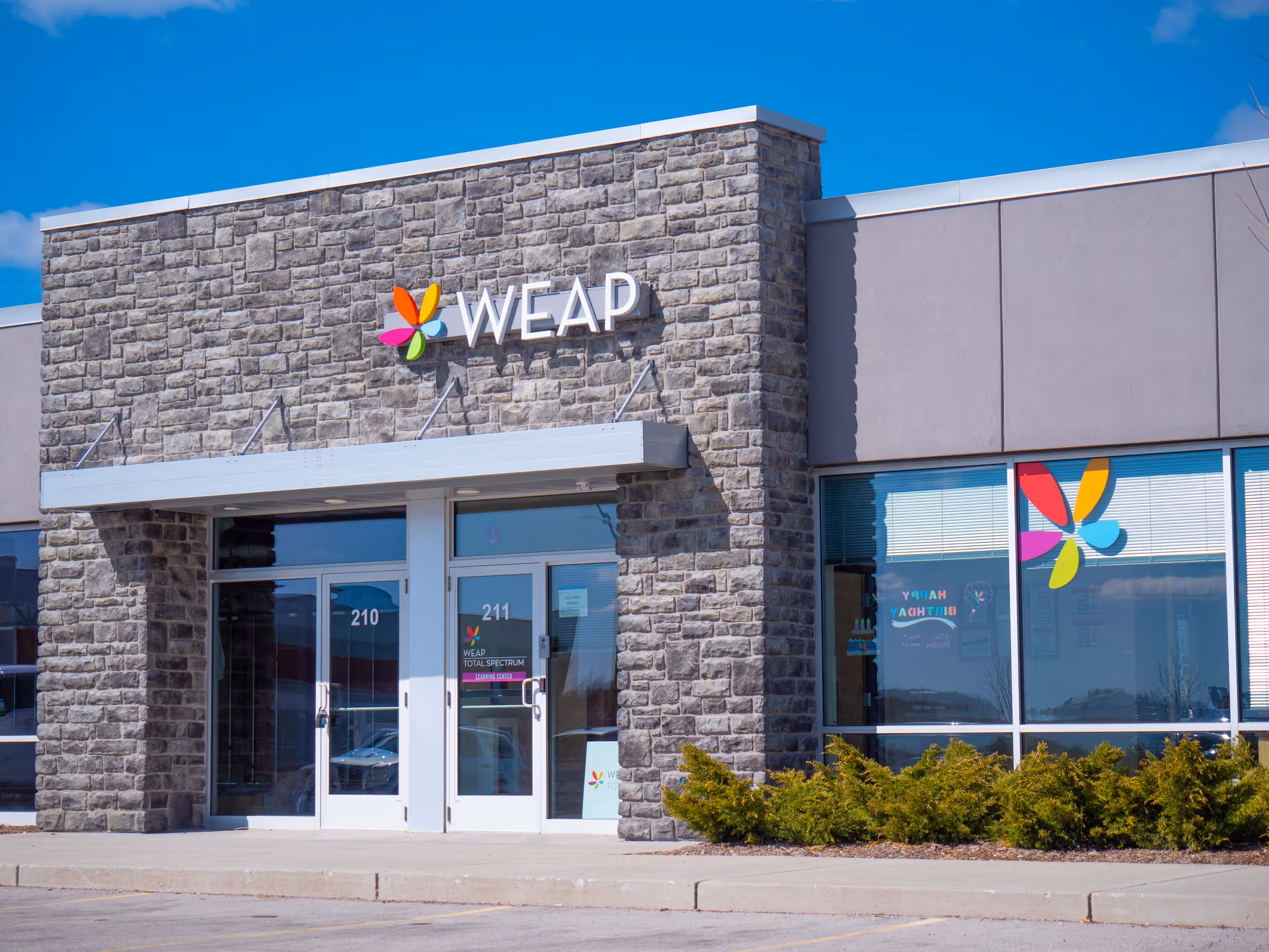 Exterior view of a stone-front building with glass doors and a colorful WEAP sign.