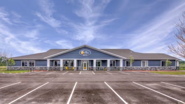 Exterior of BeeHive Homes senior living facility with a blue facade, central entrance, and empty lot.