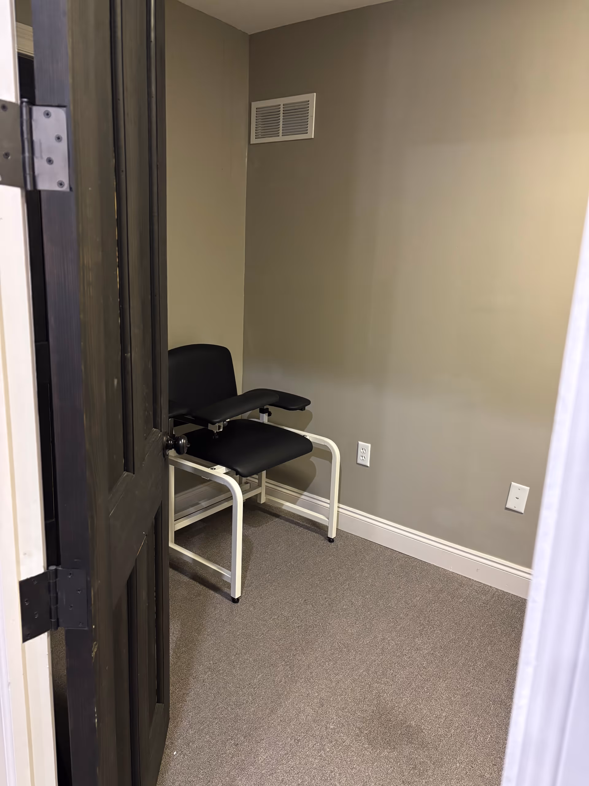 Small empty room with two black chairs, gray walls, vent, and a doorway.