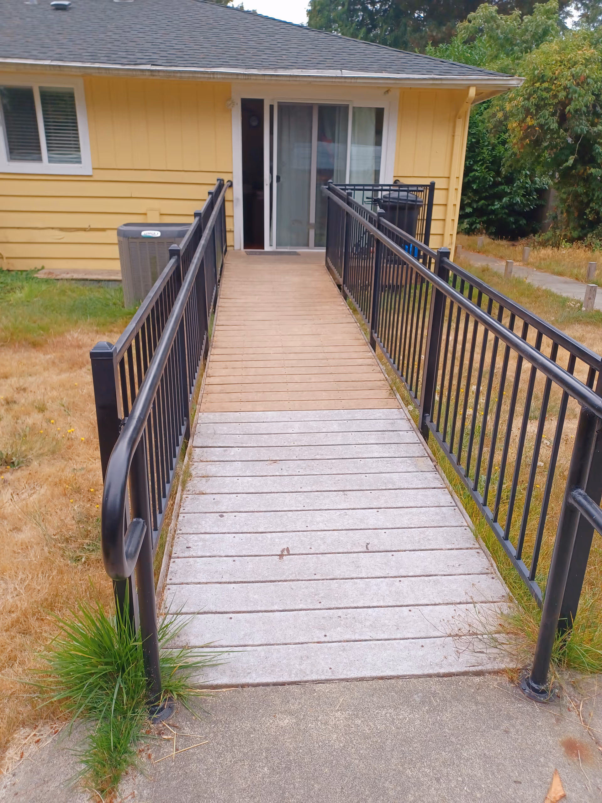 Ramp with black rails leads to a sliding glass door at a yellow facility exterior.