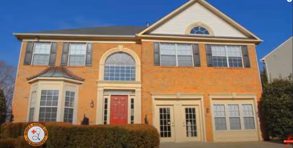 Two-story brick senior living facility exterior with red entrance door and large front windows.