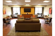 A warm, spacious senior living lounge with sofas, chairs, and a central coffee table.