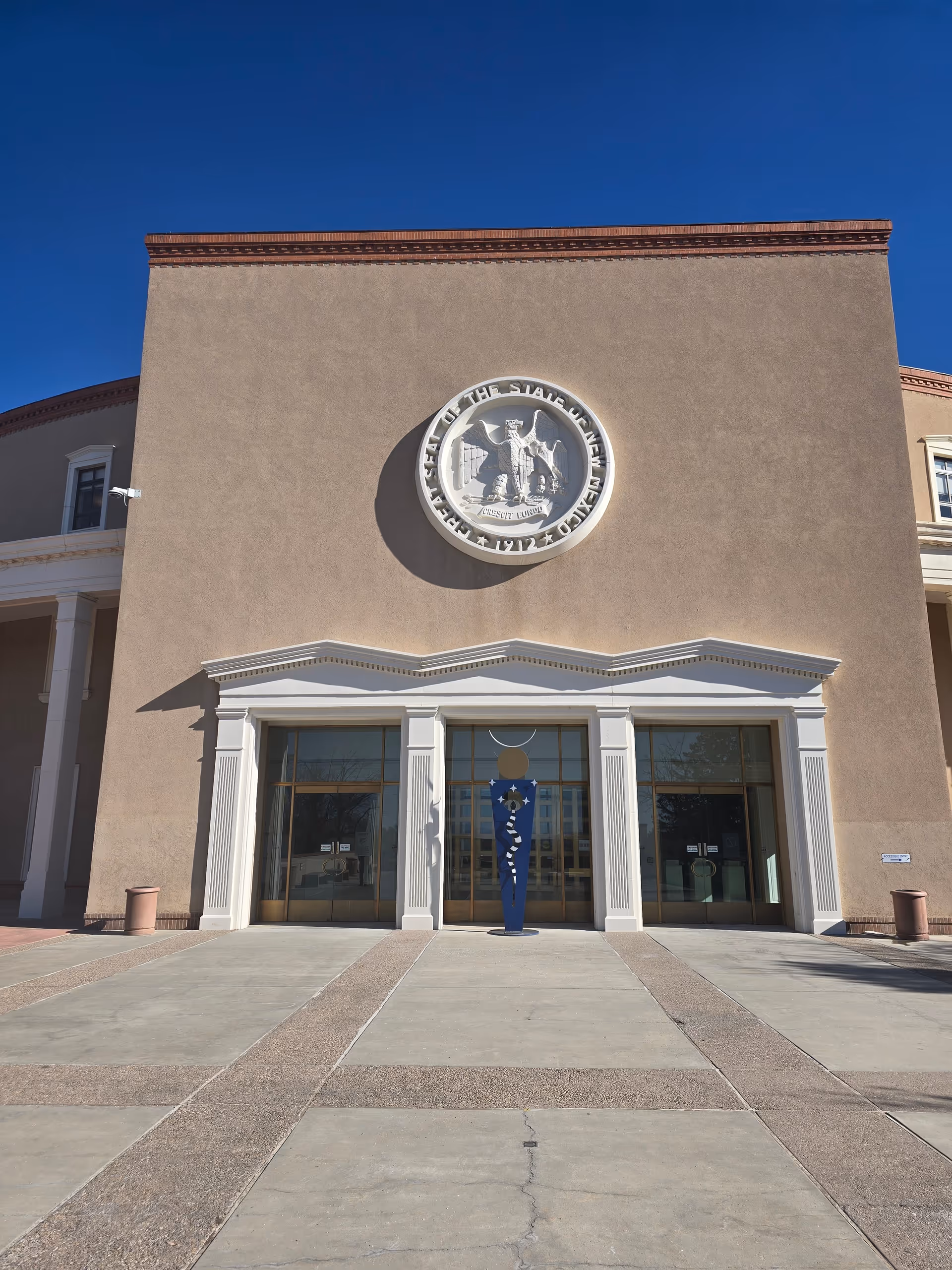 Front view of a beige building with a large circular emblem above glass doors.