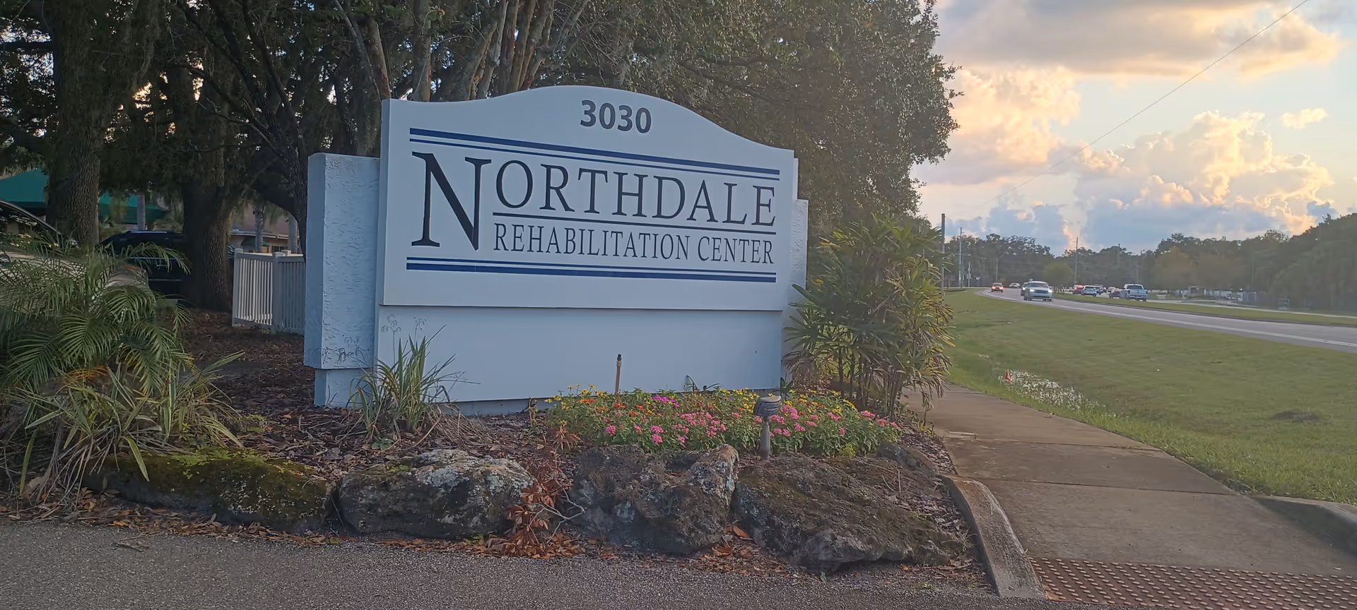 Exterior sign for Northdale Rehabilitation Center beside a landscaped entrance by the road