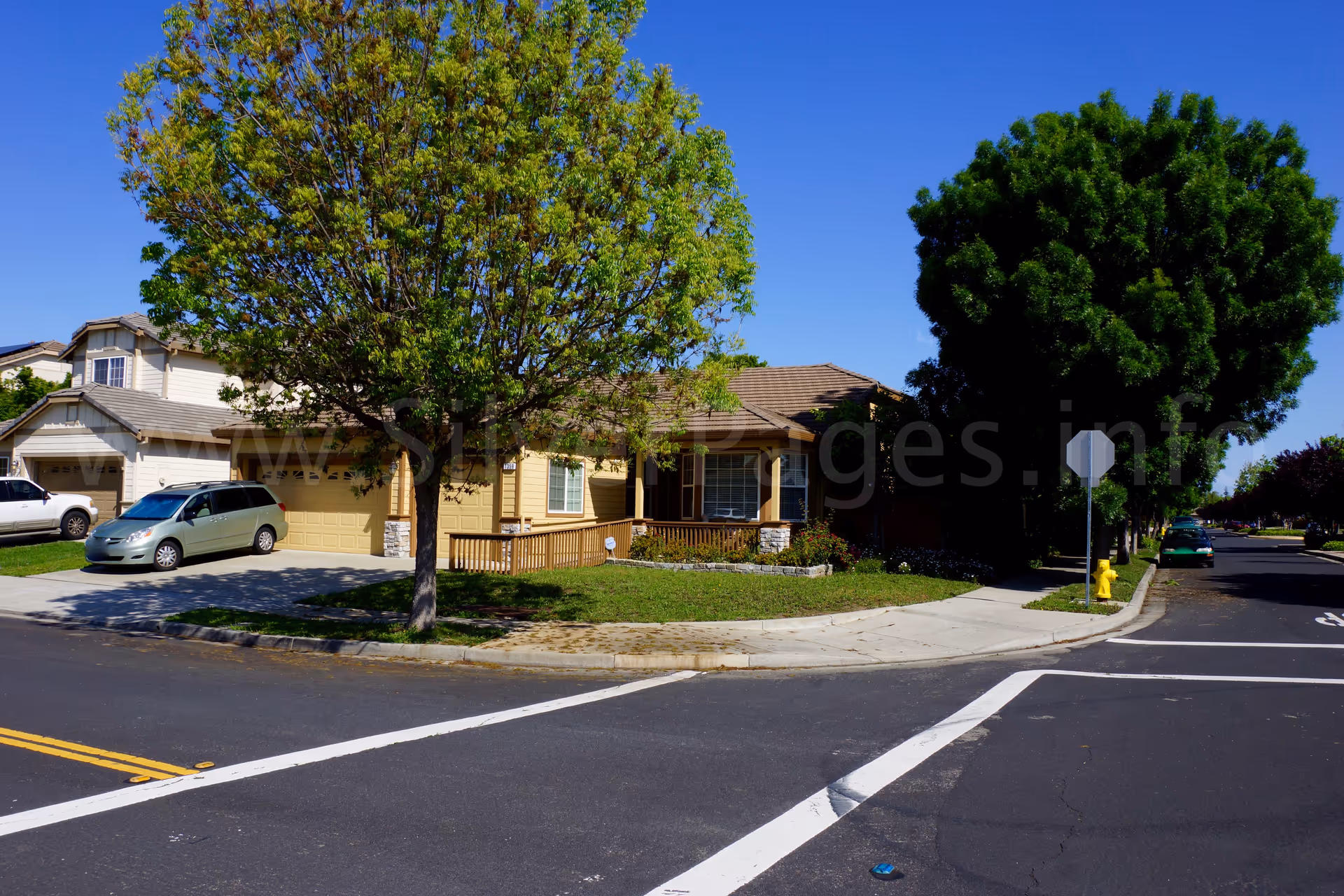 A single-story beige senior living building on a street corner with trees and parked cars.