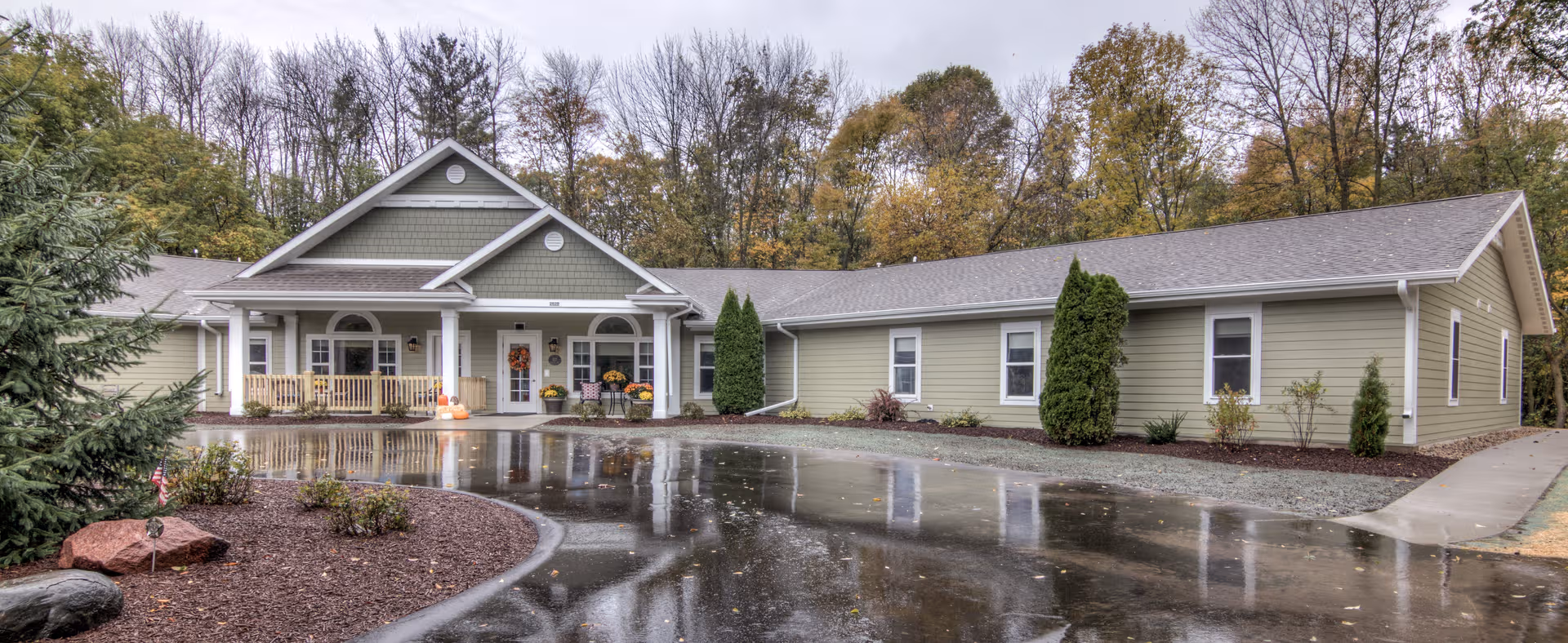 Dimensions Living Sheboygan exterior: single-story beige facility with front porch and wet driveway.