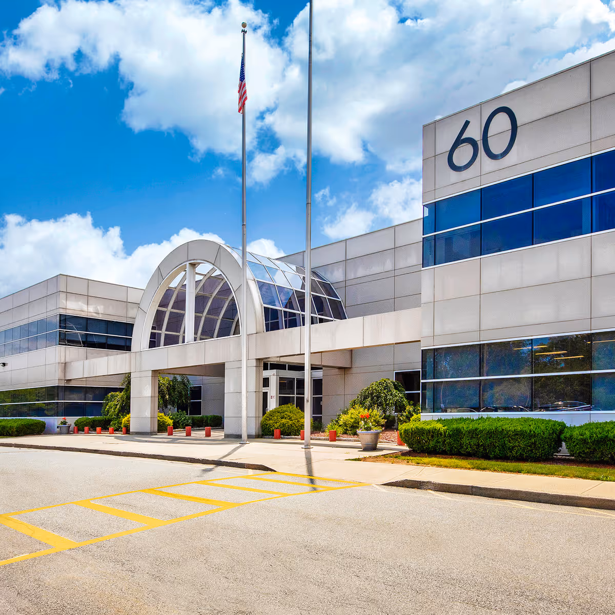 Modern medical facility with curved glass entrance, flagpole, and parking under a blue sky.