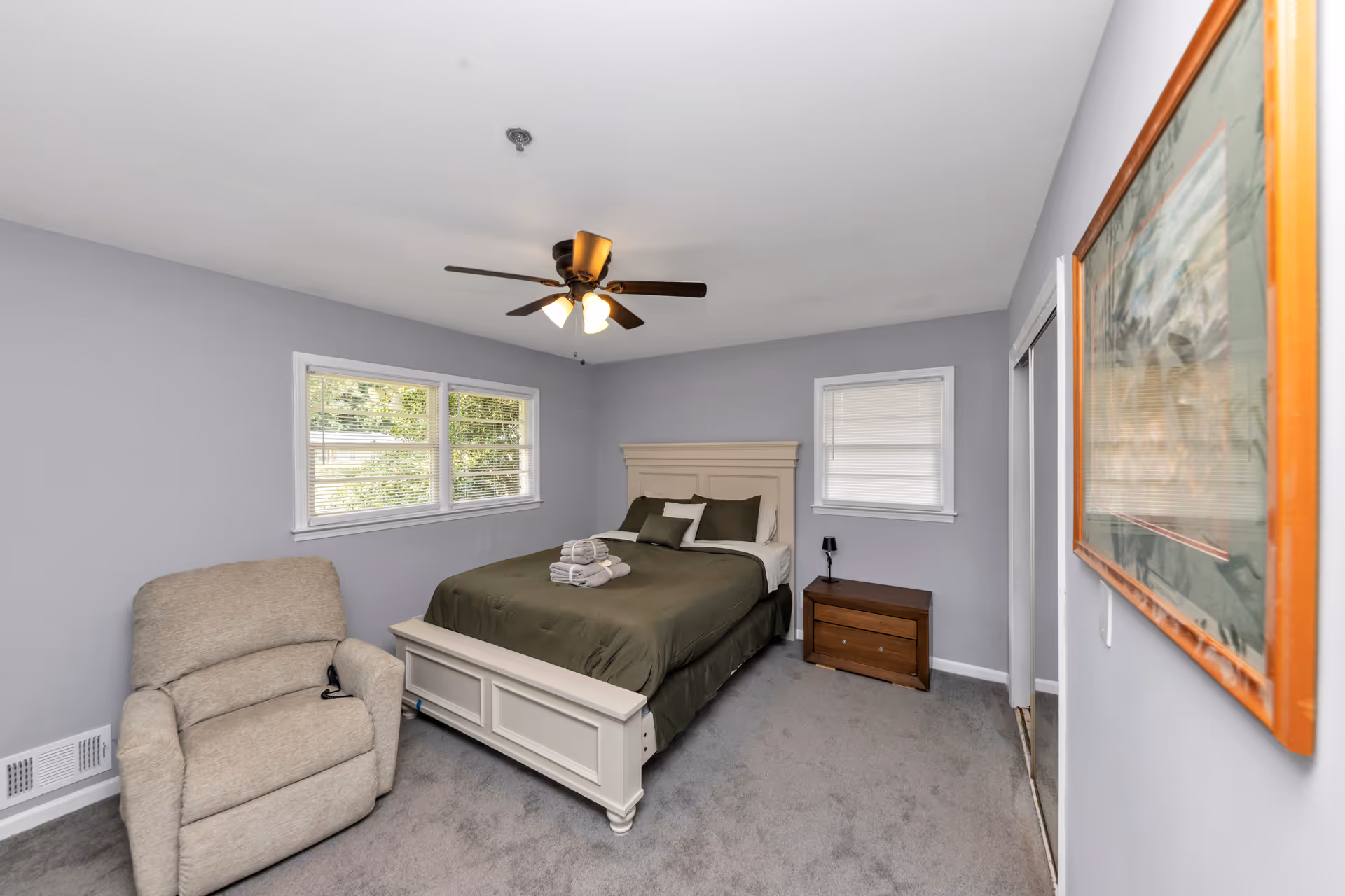 Cozy bedroom featuring a bed, nightstand, recliner, and a ceiling fan.