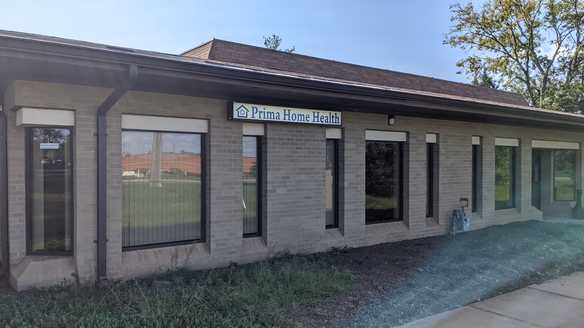 One-story brick facility with a sign reading Prima Home Health beside large windows.