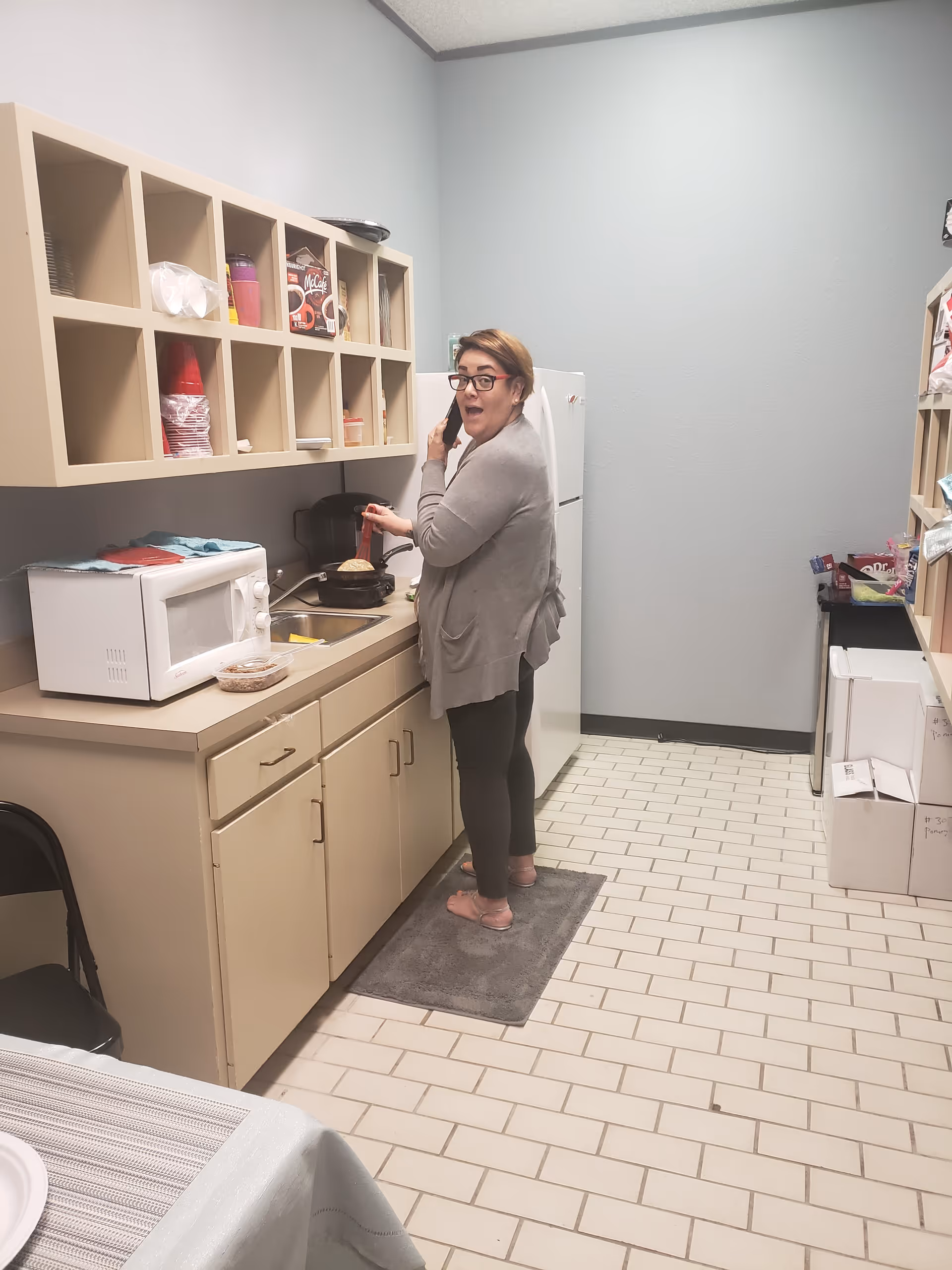 A woman stands in a compact kitchen area, cooking on the stove, talking on the phone.