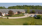 Single-story brick nursing facility with curved driveway, manicured lawn, and parked cars.