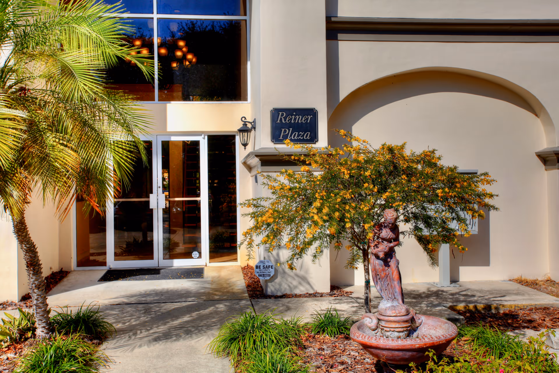 Exterior view of the entrance to Reiner Plaza with palm tree and fountain statue.