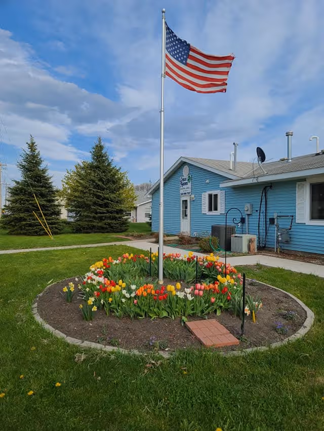Blue single-story building with flagpole, a circular tulip garden, and Grace Haven sign.