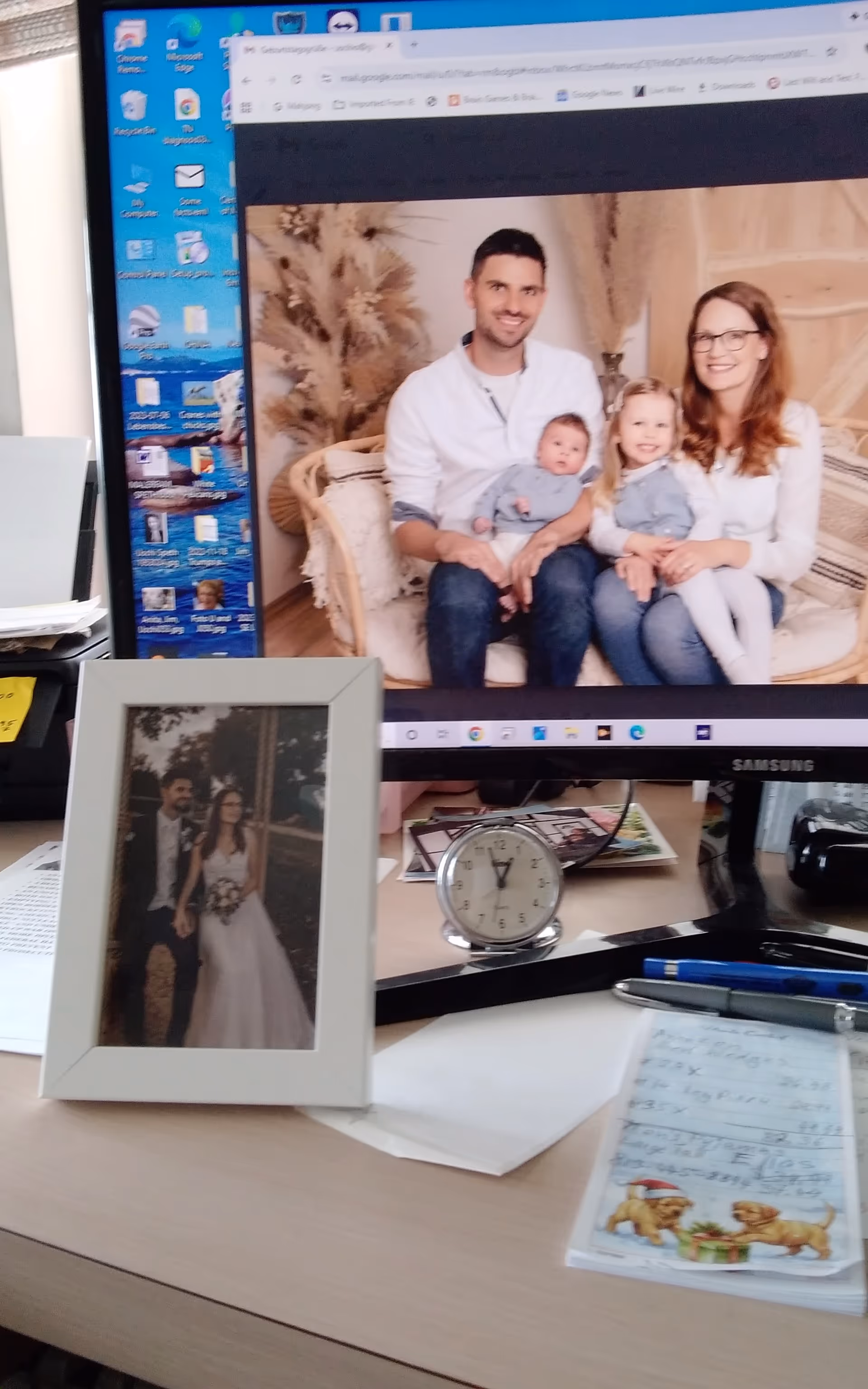 Desktop monitor displays a family photo; framed picture and a clock sit on the desk.