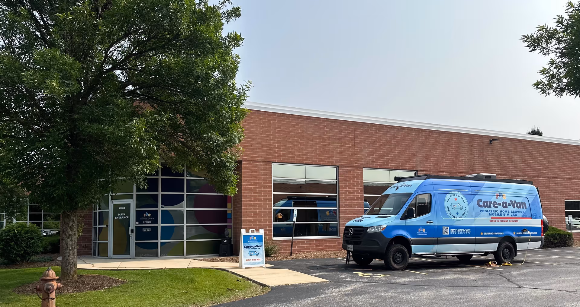 Brick facility with large glass entrance and a blue Care-a-Van parked outside.