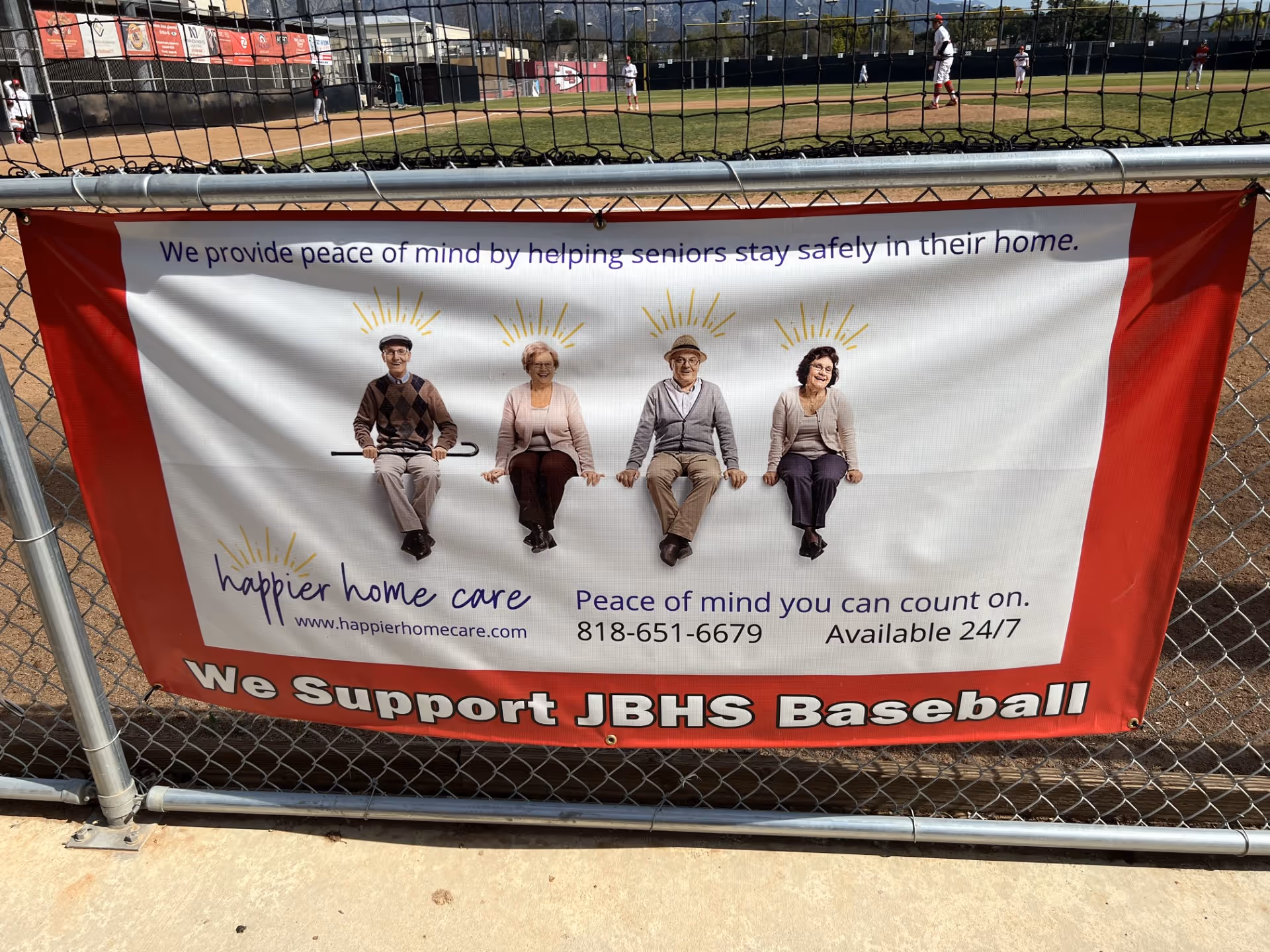 Banner on chain-link fence advertising Happier Home Care with seniors seated.