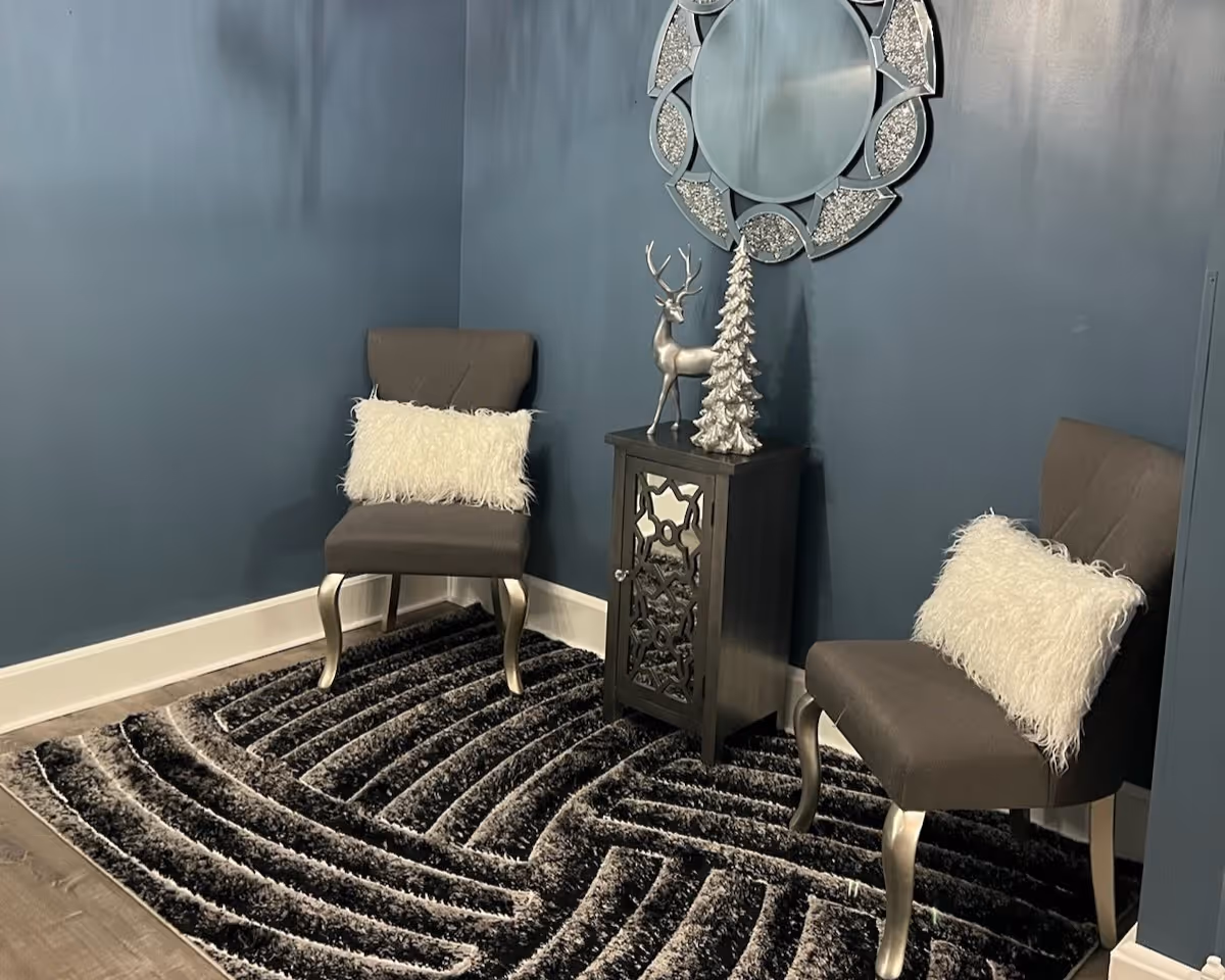 Blue-walled seating nook with two chairs, a decorative cabinet, and a round mirror.