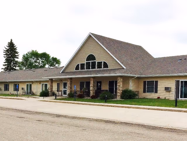 Single-story senior living facility with tan siding and a prominent gabled front entrance.