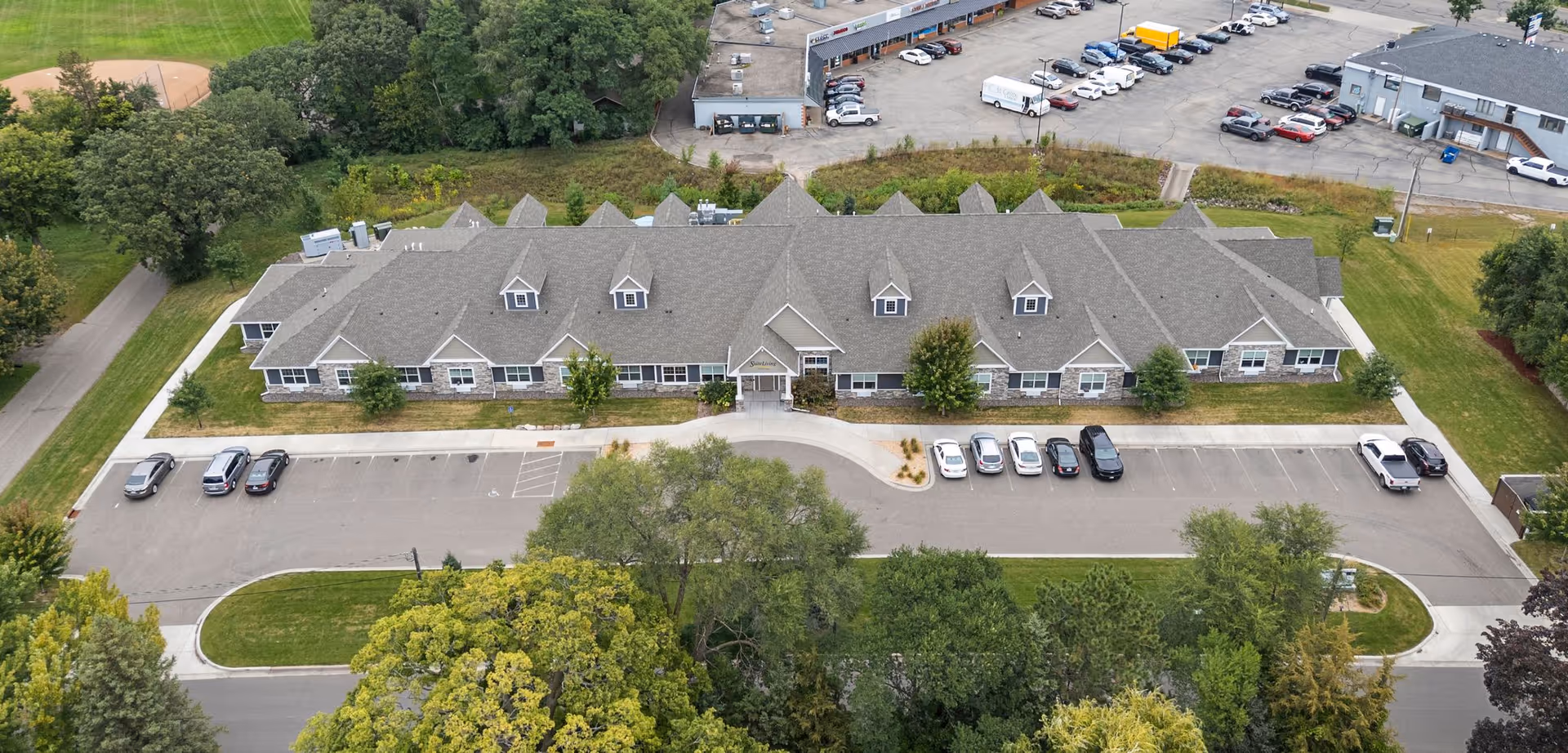 Aerial view of Suite Living of Anoka front facade with parking and surrounding trees.
