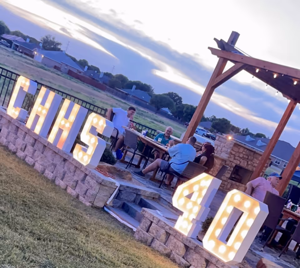 Outdoor patio with stone seating, string lights, large illuminated letters, and residents dining together.