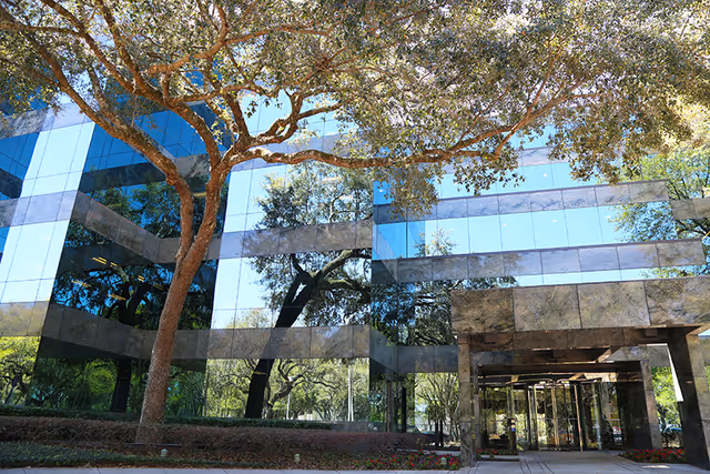 Glass-front building entrance with reflective windows and surrounding trees
